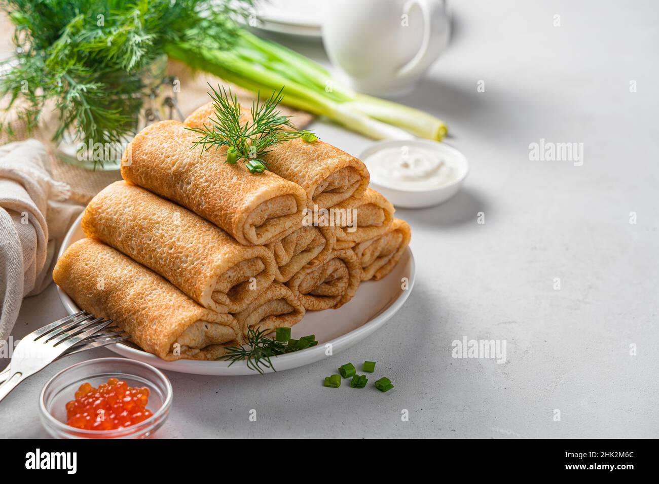 Crêpes farcies aux herbes fraîches, caviar rouge et crème aigre sur un fond clair.Vue latérale, espace de copie.Crêpes russes traditionnelles.Jour de crêpe. Banque D'Images