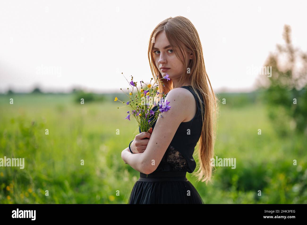 Portrait d'une fille russe avec un bouquet de fleurs sauvages dans la soirée au village. Banque D'Images