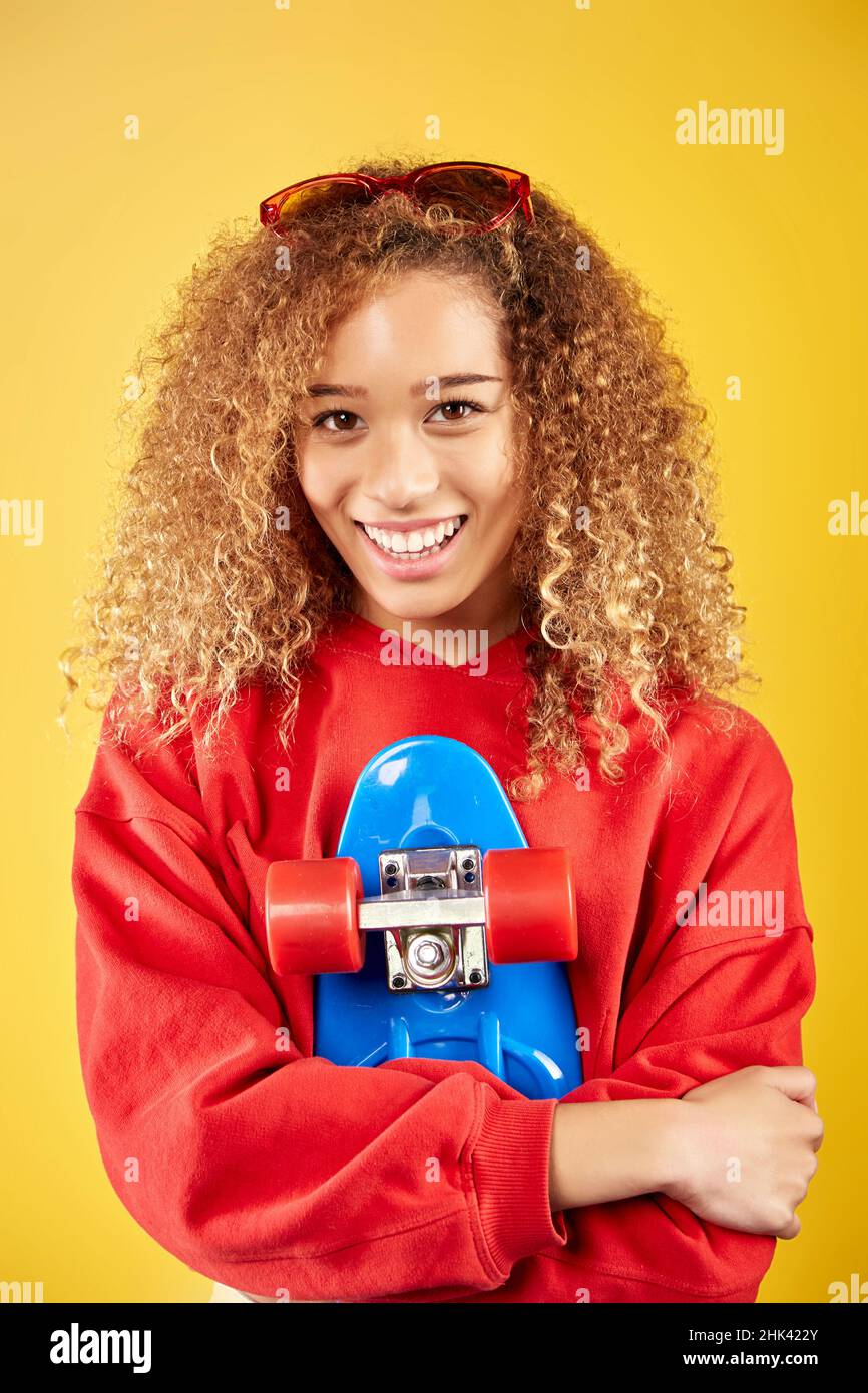 Ravie de jeunes Afro-américaines hipster dans le sweat à capuche et avec panneau de penny regardant la caméra sur fond jaune Banque D'Images