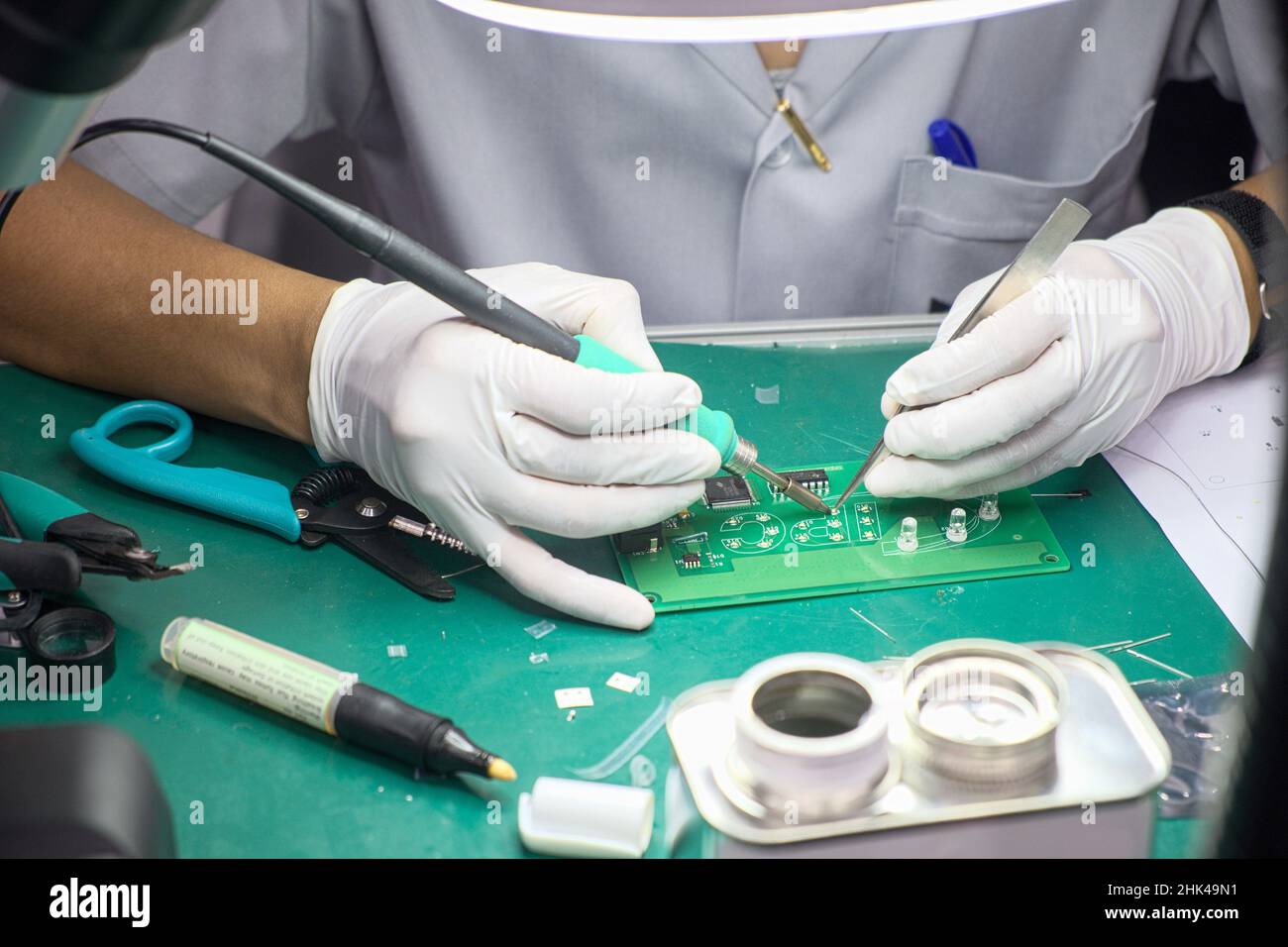 Une femme de technicien en gros plan sur des gants en caoutchouc et une combinaison de travail utilise la soudure pour souder la carte de circuit électronique sur le bureau Banque D'Images