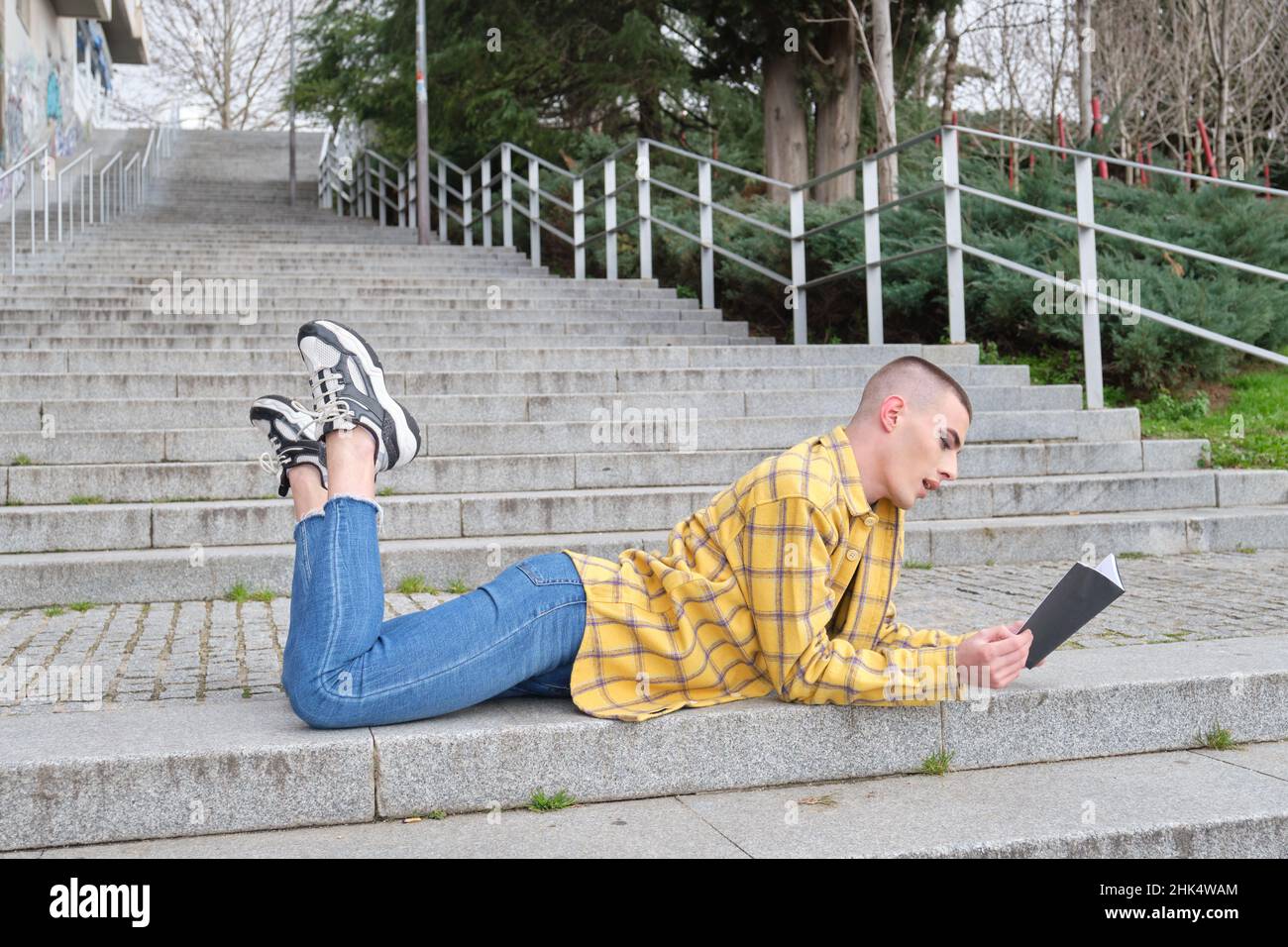 Jeune personne non binaire allongé sur les escaliers et lisant un livre. Banque D'Images