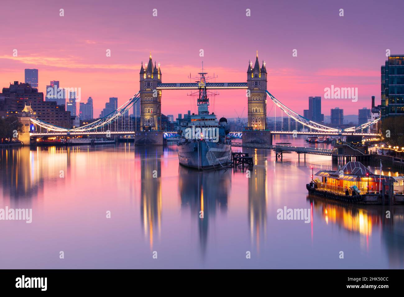 Vue au lever du soleil sur le HMS Belfast et le Tower Bridge se reflétant dans la Tamise, avec Canary Wharf en arrière-plan, Londres, Angleterre, Royaume-Uni, Europe Banque D'Images