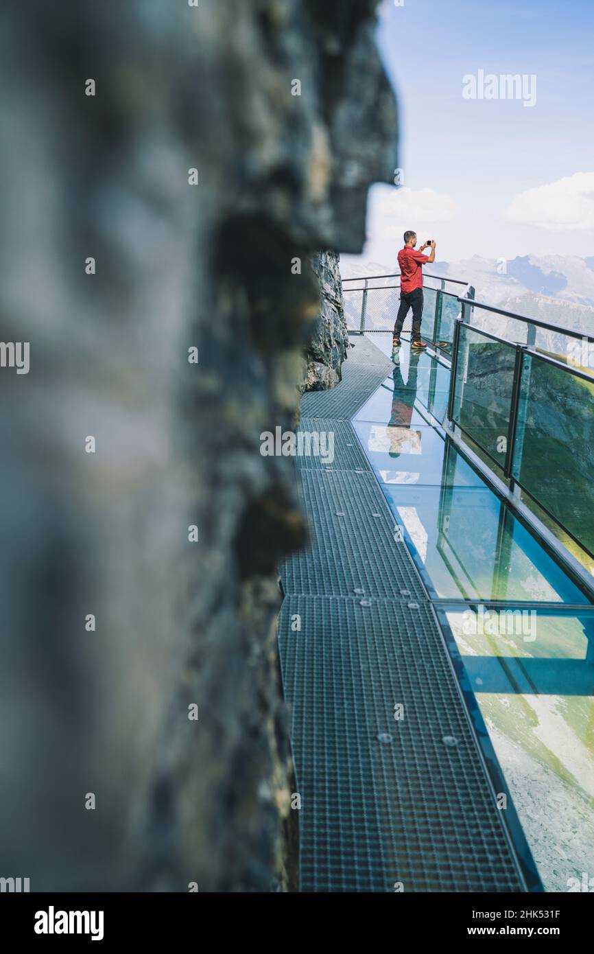 Homme photographiant des montagnes avec un smartphone depuis la passerelle panoramique en verre de la randonnée à sensations fortes, Murren Birg, canton de Berne, Suisse, Europe Banque D'Images