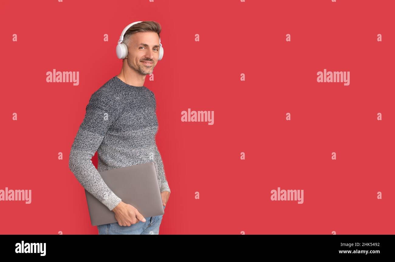 Homme heureux dans une ambiance décontractée écouter des cours audio en ligne dans un casque tenant un ordinateur portable, e-éducation Banque D'Images