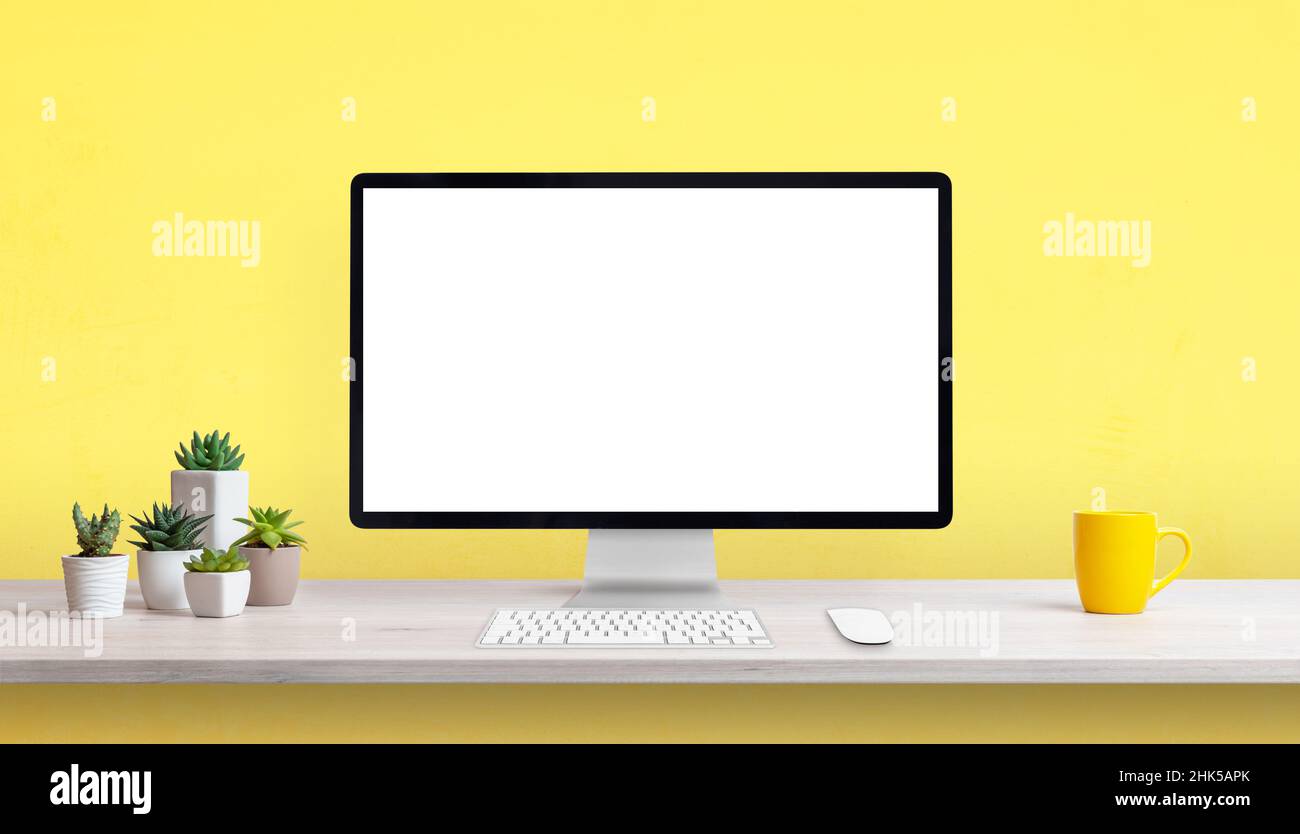 Bureau de travail créatif avec écran d'ordinateur vierge, tasse à café jaune et plantes.Arrière-plan jaune avec espace de copie Banque D'Images