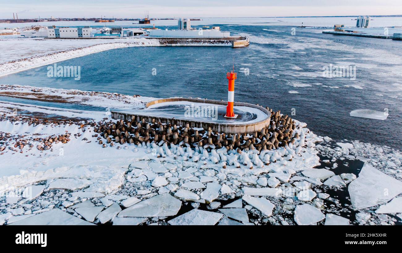 L'eau de mer claire, froide et sombre, et les grandes pièces de glace cassées entourent le territoire clos d'un phare rouge-blanc lumineux défendu par le panorama aérien des brise-lames Banque D'Images