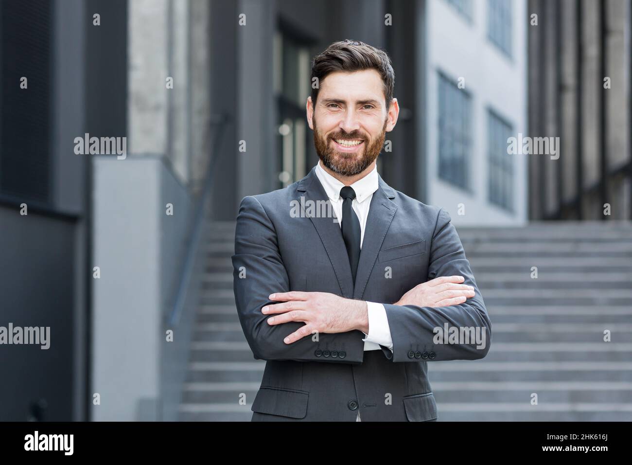 Homme d'affaires prospère et joyeux regardant l'appareil photo et souriant, portrait avec les bras croisés près du bureau Banque D'Images