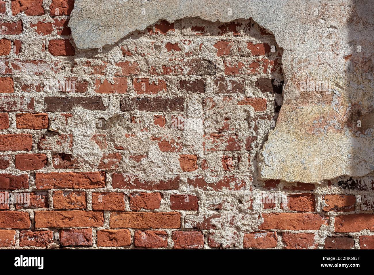 Fragment d'un mur de briques rouges partiellement recouvert de plâtre en fricleur pour une utilisation comme fond abstrait et texture. Banque D'Images