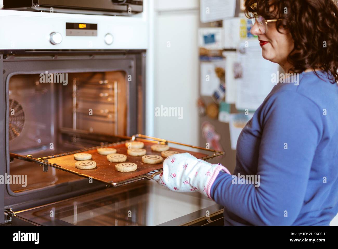 Femme caucasienne dans la cuisine mettant un plateau avec des biscuits dans le four.Cuisson à la maison.Mise au point sélective. Banque D'Images