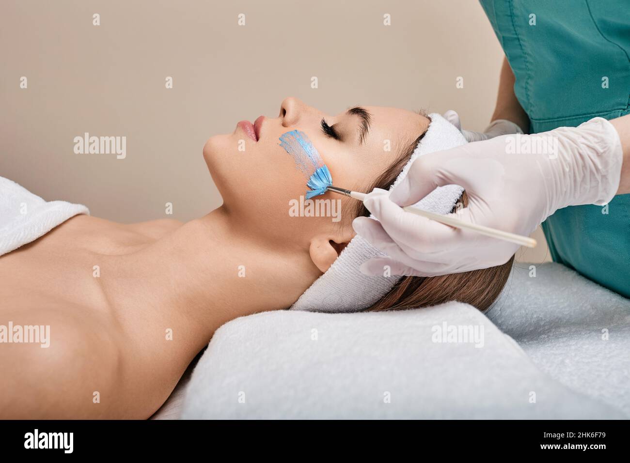 Esthéticienne applique le masque de soin sur le visage de la femme à l'aide d'une brosse de cosmétologie. soins de la peau du visage avec masque cosmétique à la clinique de beauté Banque D'Images