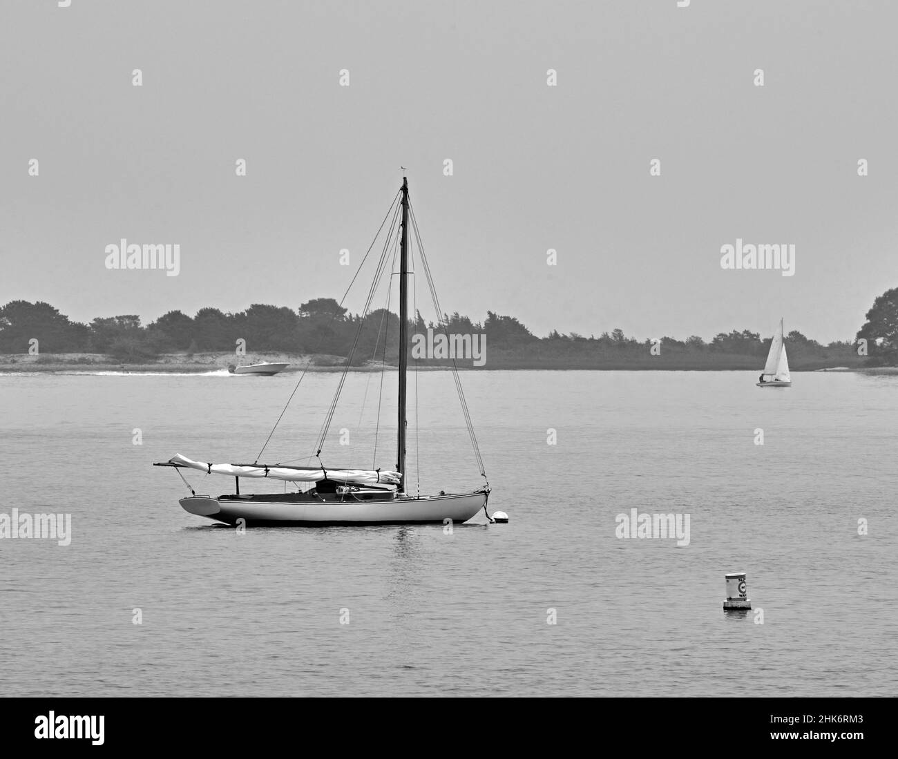 Un seul bateau avec une voile sur Lewis Bay à Cape Cod, Massachusetts.USA, un jour gris. Près du port de Hyannis. En noir et blanc. Banque D'Images