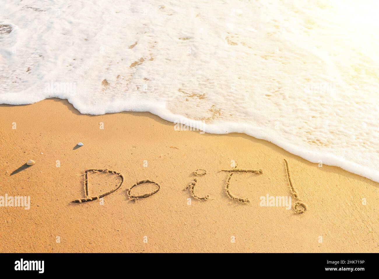 Mot « Do IT » écrit sur le sable de la plage.Message positif écrit sur le bord de mer au coucher du soleil Banque D'Images