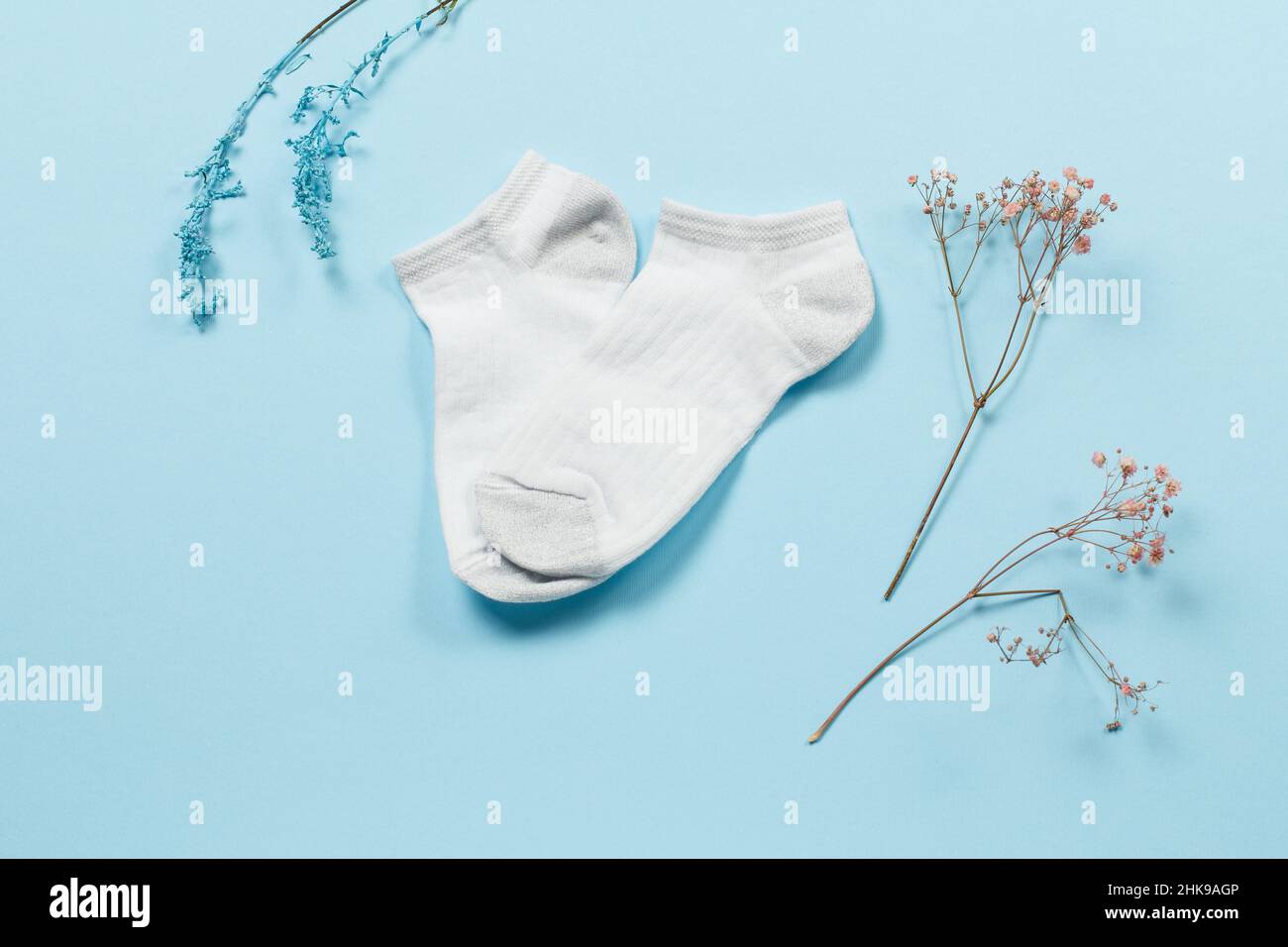 Paire de chaussettes blanches pour femmes et branches décoratives sur fond bleu, vue du dessus. Banque D'Images