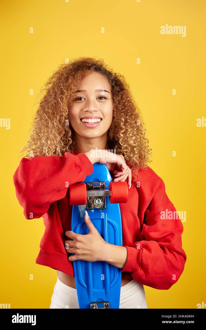 Ravie de jeunes Afro-américaines hipster dans le sweat à capuche et avec panneau de penny regardant la caméra sur fond jaune Banque D'Images