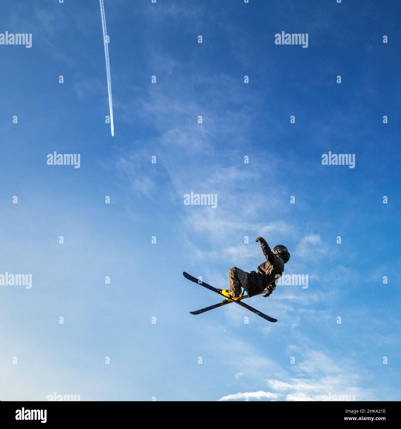 Saut à ski volant haut dans l'air sur fond bleu ciel avec une trace d'un avion à réaction. Banque D'Images