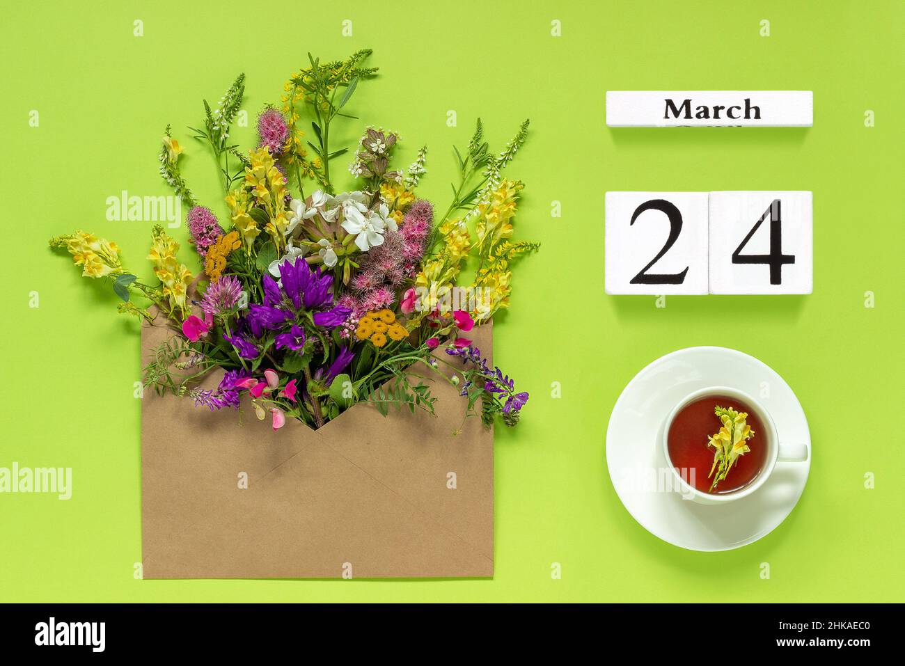 Calendrier des cubes en bois Mars 24.Tasse de thé aux herbes, enveloppe kraft avec fleurs multicolores sur fond vert.Concept Hello Spring Creative Top vie Banque D'Images