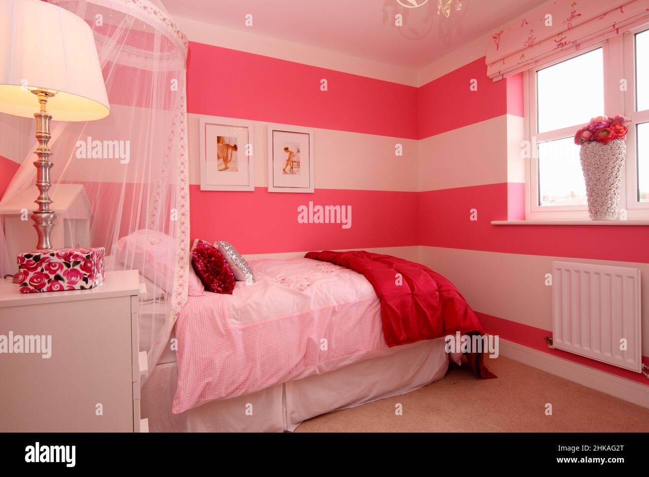 Chambre de filles rose et blanche, lit couronne à baldaquin, photos de danseuses sur le mur, lampe de chevet. Banque D'Images