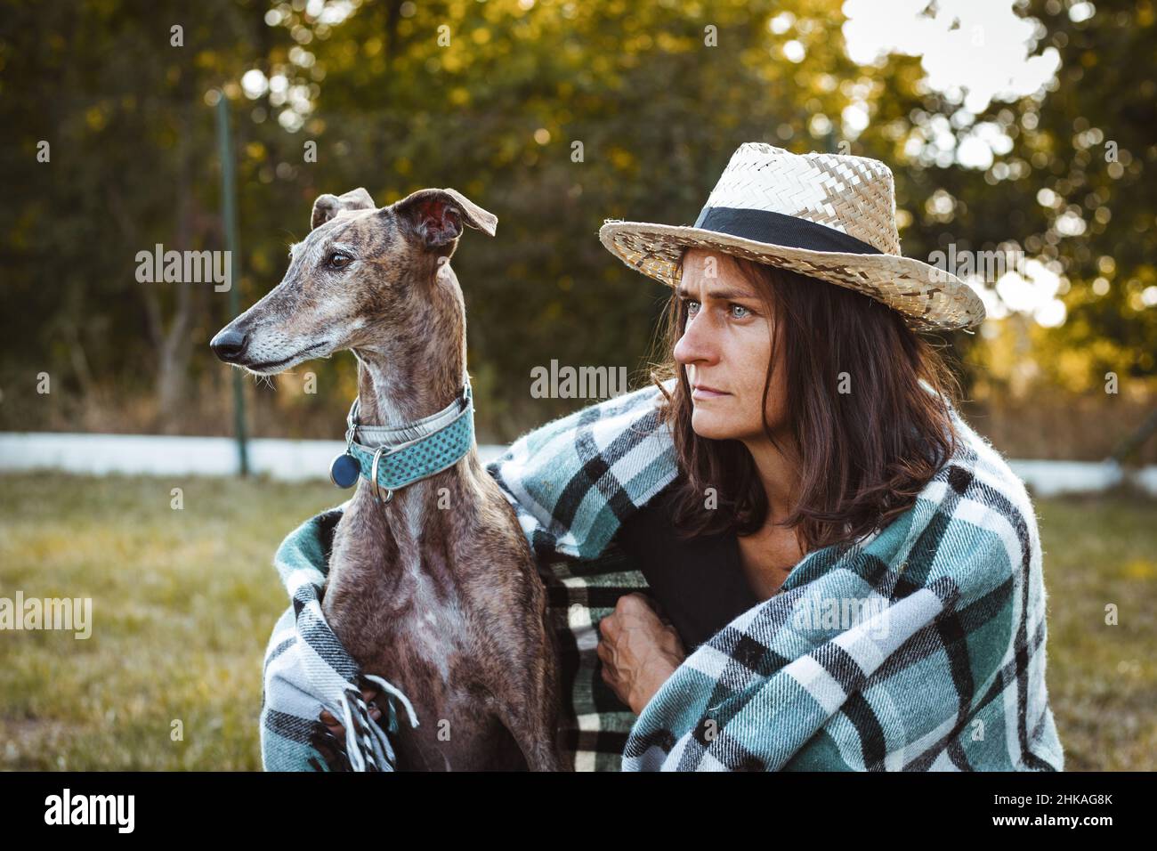 Femme avec son chien assis dans le jardin enveloppé d'une couverture.Galgo espagnol avec le propriétaire de l'animal Banque D'Images
