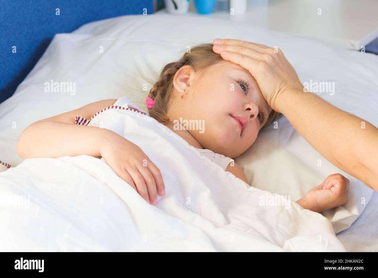 Femme main sur le front de l'enfant pour sentir la température.Un enfant de race blanche de trois ans est au lit Banque D'Images