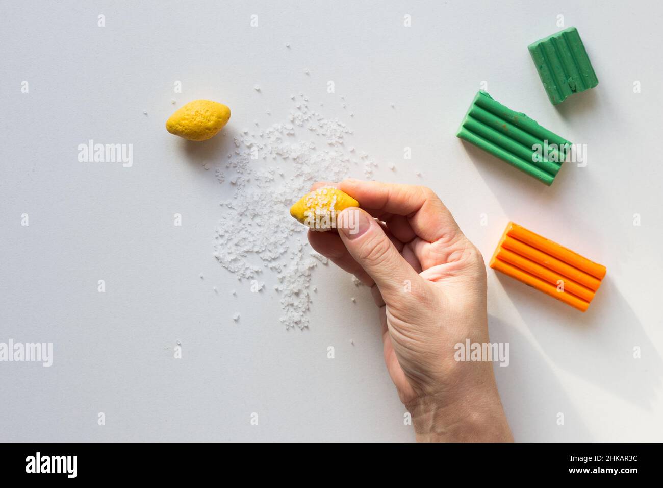 Petit citron fait d'argile polymère avec sel de mer pour faire des bosses comme sur le vrai fruit de citron dans la main de femme sur fond blanc Banque D'Images