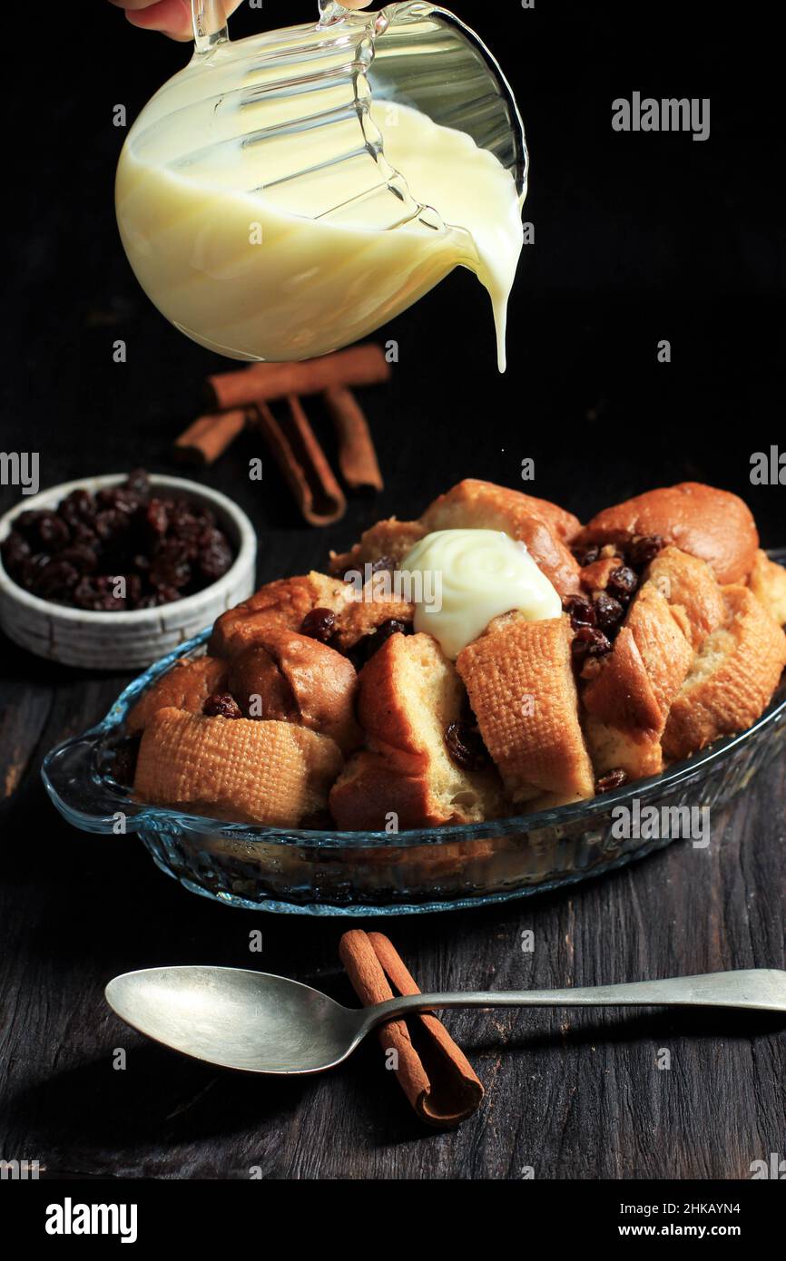 Versez la vanille VLA dans le pudding de pain frais fait de baguette en tranches avec raisin et cannelle, sur la table en bois noir Banque D'Images
