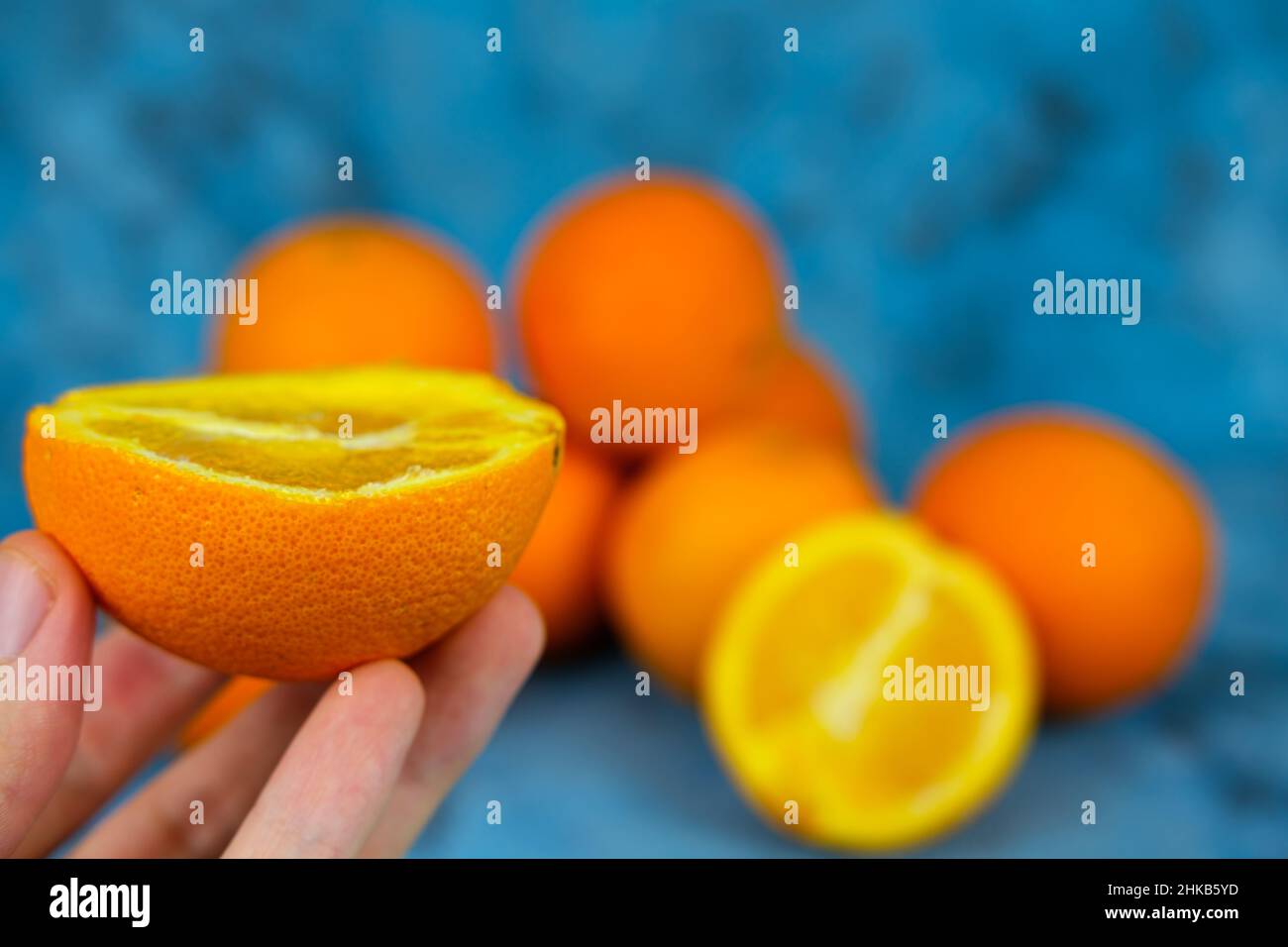 La main de la femme tient une demi-pile orange vif sur fond bleu texturé.Vue latérale ou profil de beaucoup d'oranges fraîches. Banque D'Images