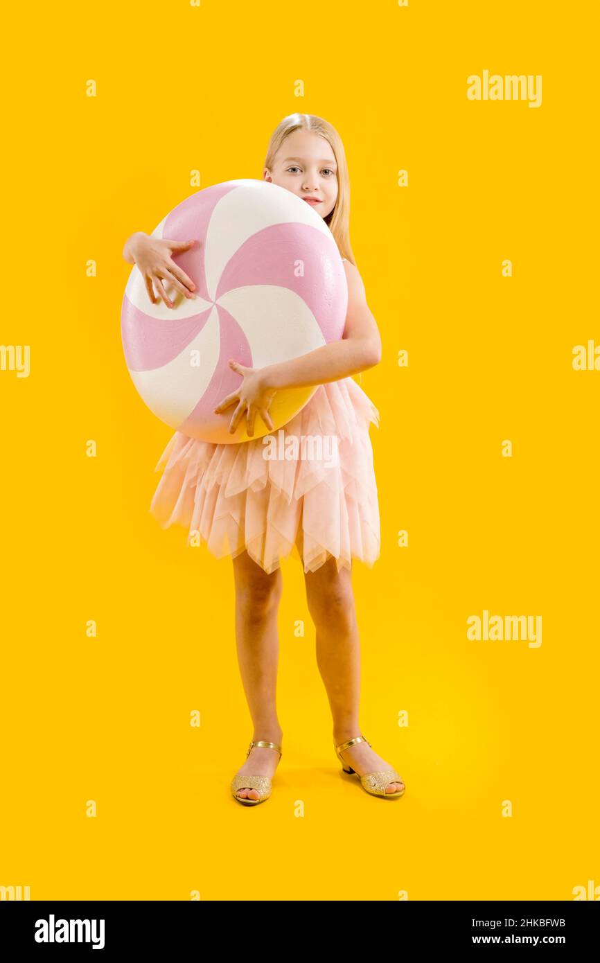 Une jolie fille tient un énorme bonbon rose et blanc sur un fond jaune.Cadeau sucré.Grand rebord.Douceur de Noël Banque D'Images