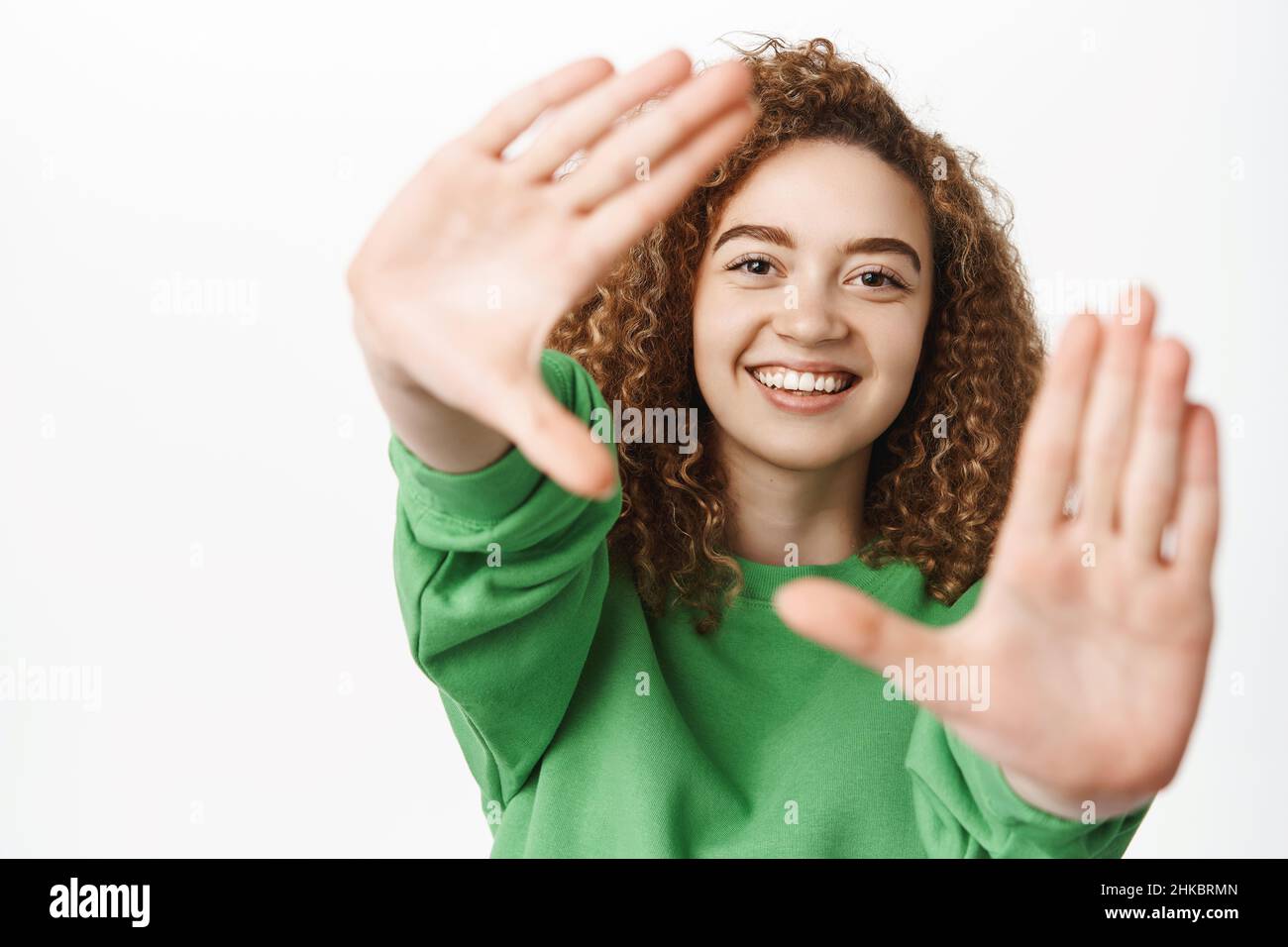 Portrait d'une belle fille heureuse, souriante, regardant à travers les cadres de doigt, capturant l'instant, prenant des photos, se tenant sur un arrière-plan blanc Banque D'Images