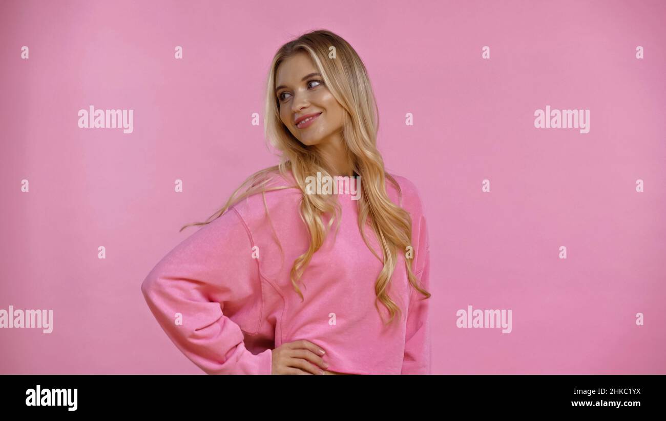 Femme souriante en sweat-shirt tenant la main sur la hanche isolée sur le rose Banque D'Images