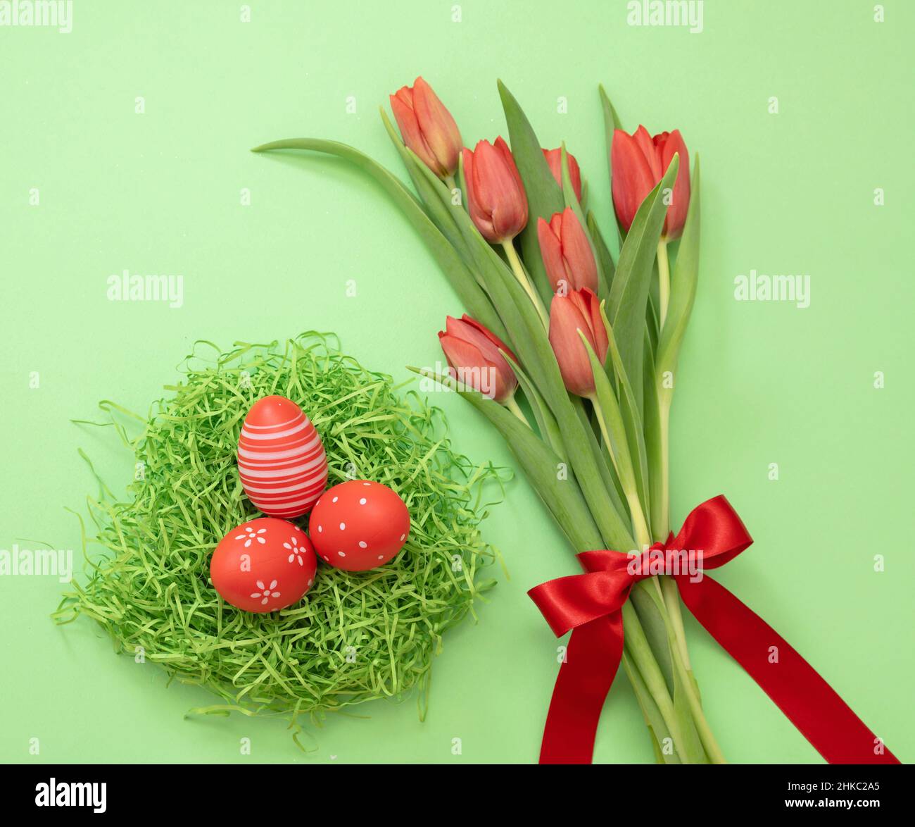 Fête du printemps de Pâques.Nid d'oeuf rouge et bouquet de tulipes frais sur fond vert pastel, vue du dessus. Banque D'Images