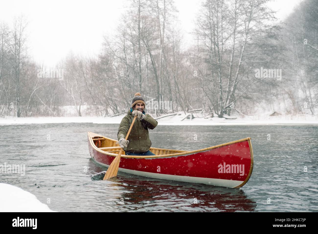 Homme souriant en canoë canadien rouge en hiver. Banque D'Images