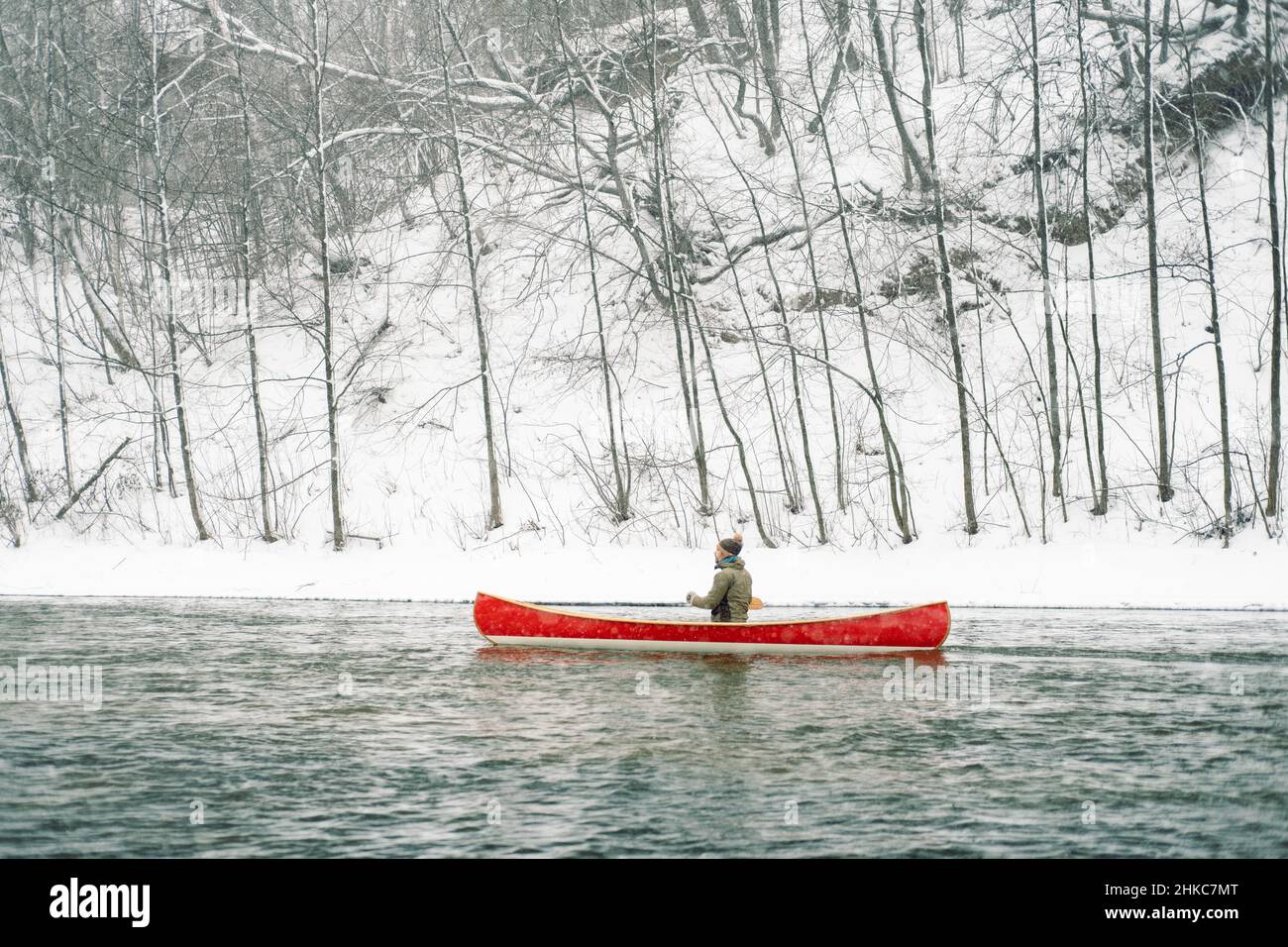 Un homme qui fait du canoë rouge canadien sur la rivière d'hiver enneigée. Banque D'Images