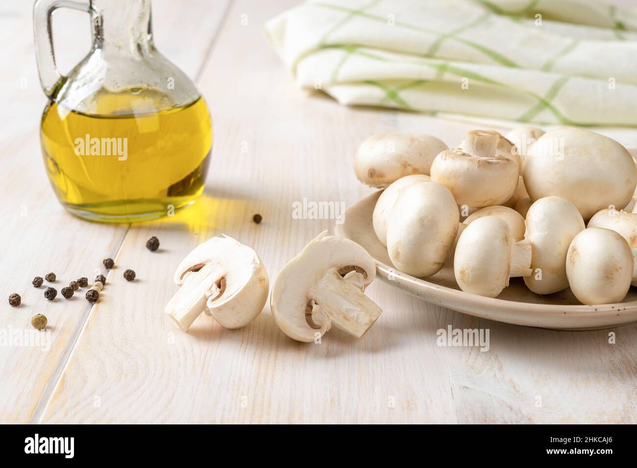 Champagnes crus sur une assiette et bocal à l'huile d'olive sur une table en bois blanc.Cuisson de champignons de Paris frais Agaricus bisporus.Concept de la cuisine végétarienne. Banque D'Images