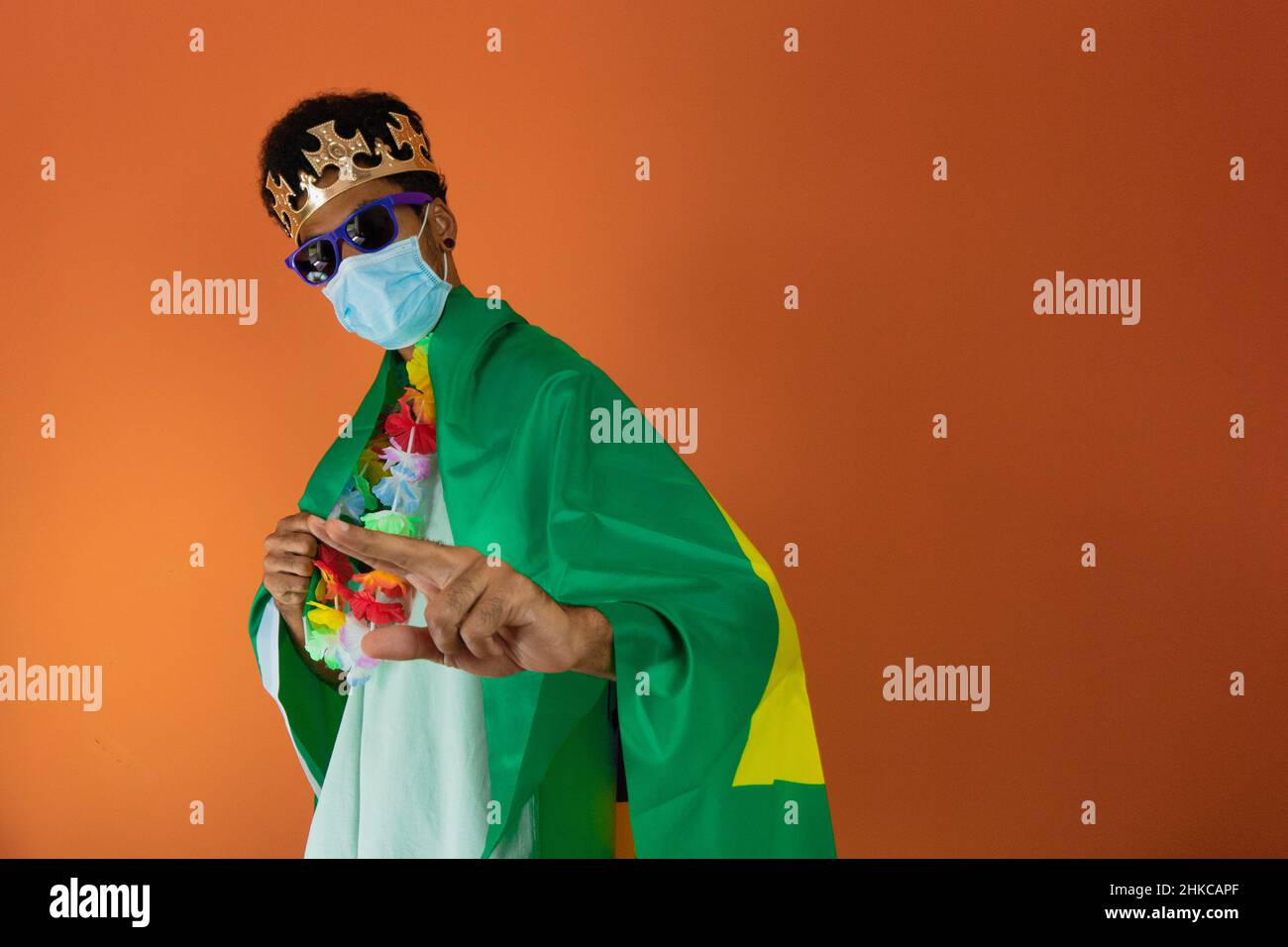 Homme noir en costume de carnaval avec masque pandémique et drapeau brésilien isolé. Banque D'Images