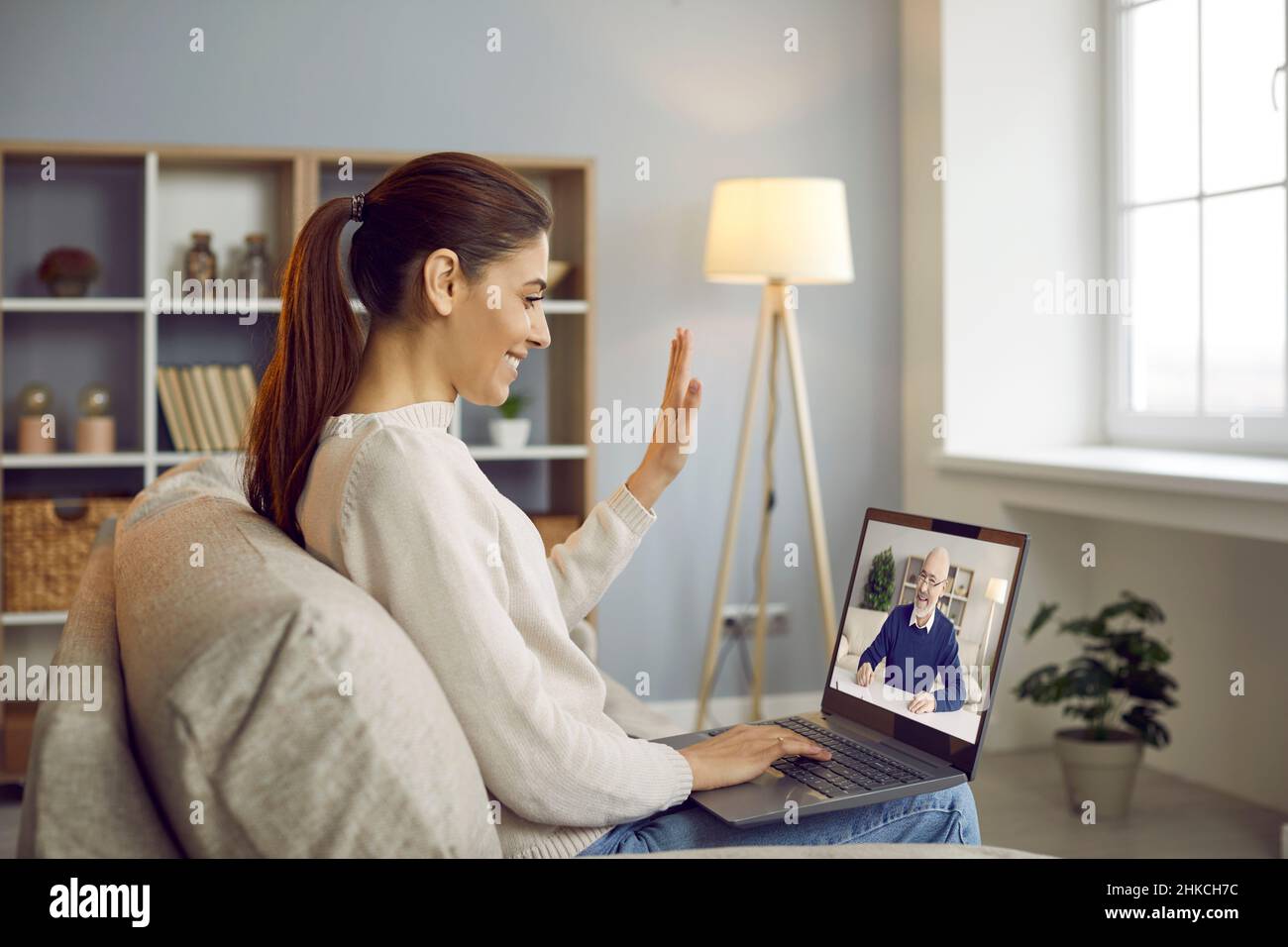 Bonne jeune femme ayant la réunion en ligne, souriant et saluant bonjour à l'écran d'ordinateur portable Banque D'Images