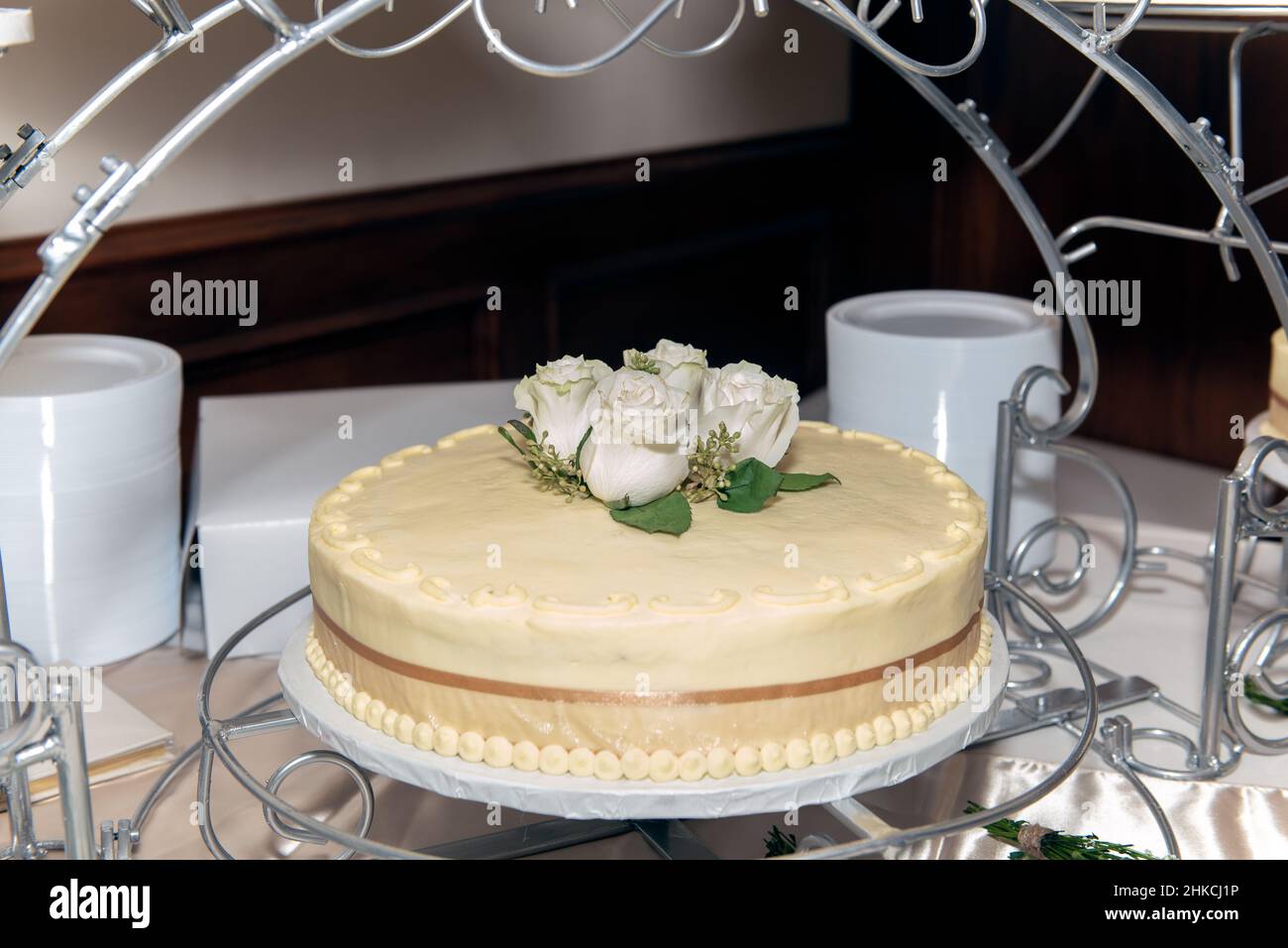 Gâteau de mariage sur un support orné de roses dépolies sur le glaçage du gâteau. Banque D'Images