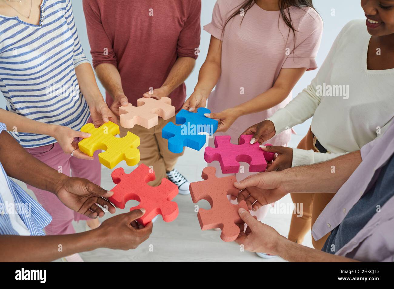 Une équipe diversifiée de jeunes hommes et femmes heureux se joignant à des pièces colorées de puzzle puzzle Banque D'Images