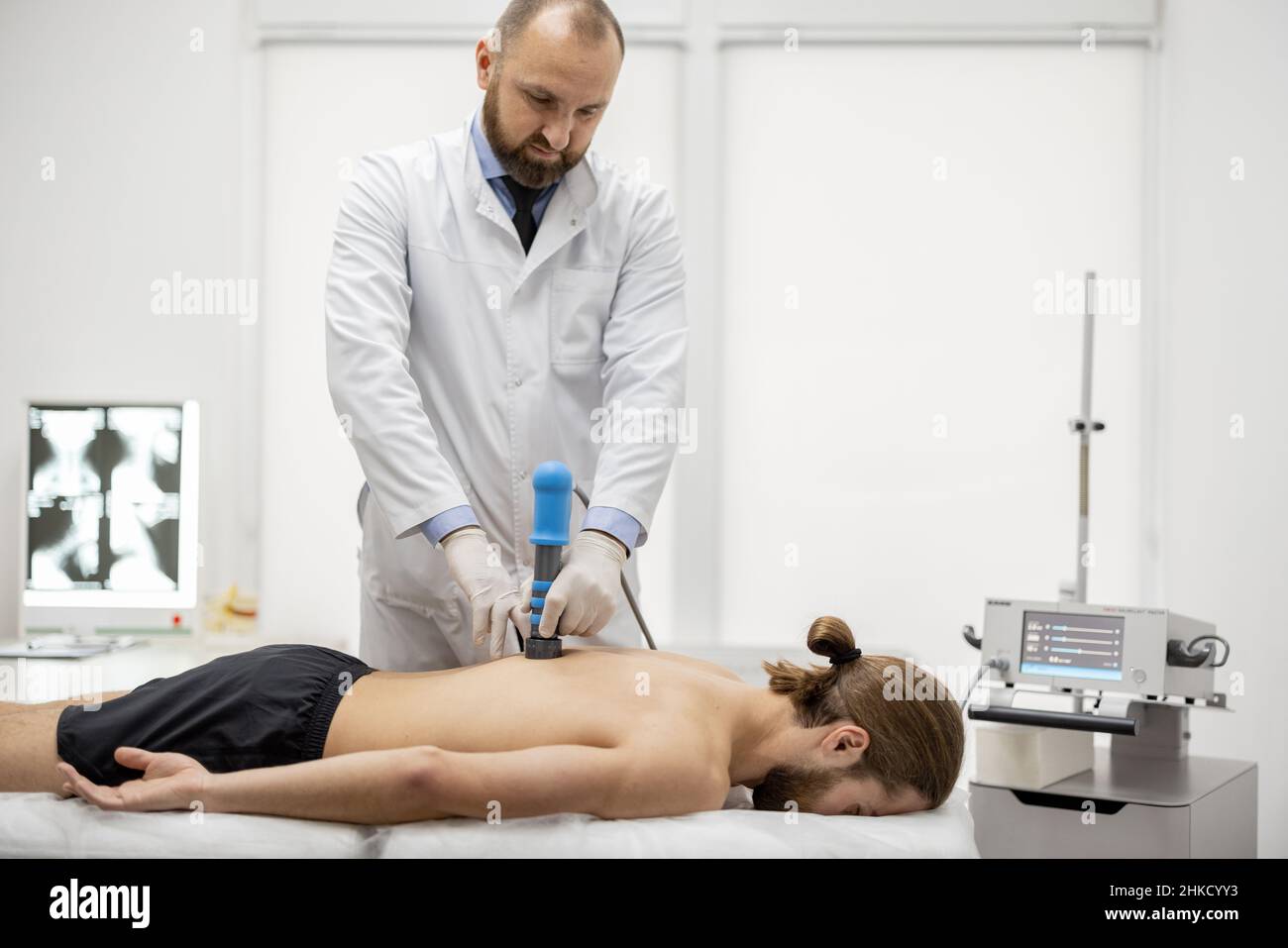 Le médecin applique un traitement par onde de choc sur l'épaule des hommes Banque D'Images