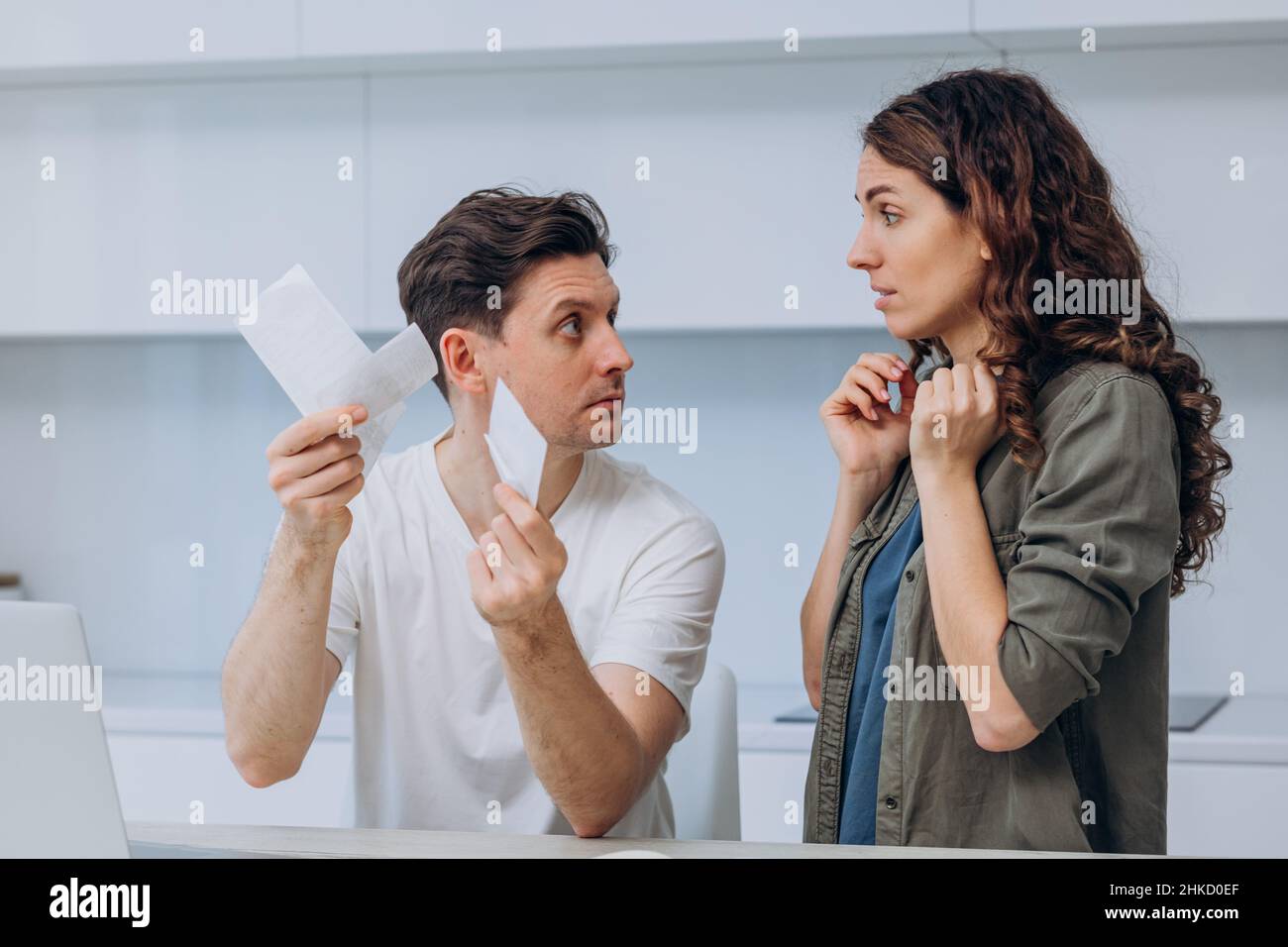 Le jeune mari et la femme discutent des sommes d'argent dans le contrôle de supermarché et arguent des dépenses à table avec ordinateur portable et calculatrice dans la cuisine Banque D'Images