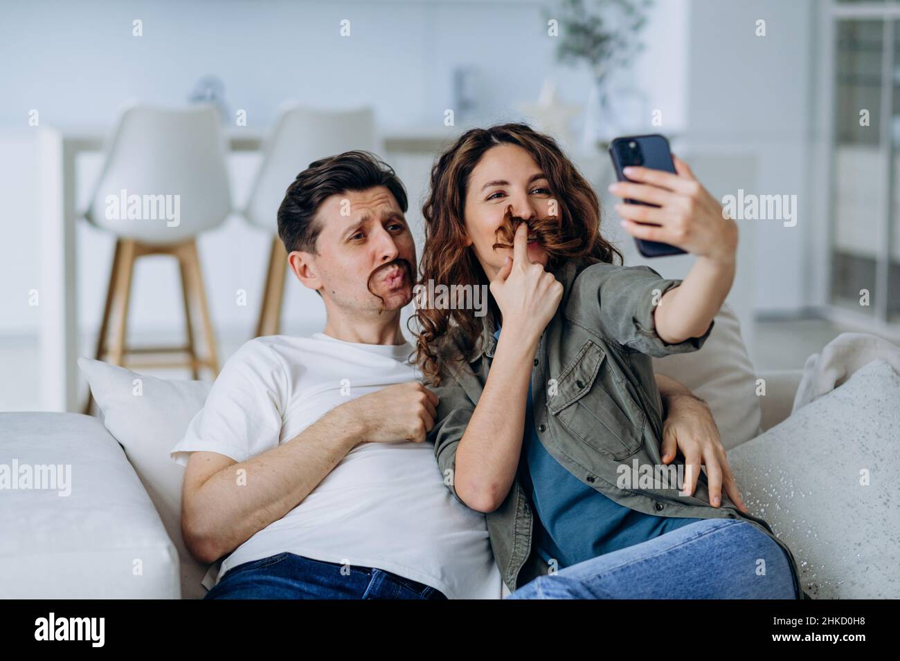 Une brune souriante et un jeune homme aux cheveux courts se posent avec des cheveux bouclés comme une moustache pour des photos et des vidéos souriantes gros plan Banque D'Images