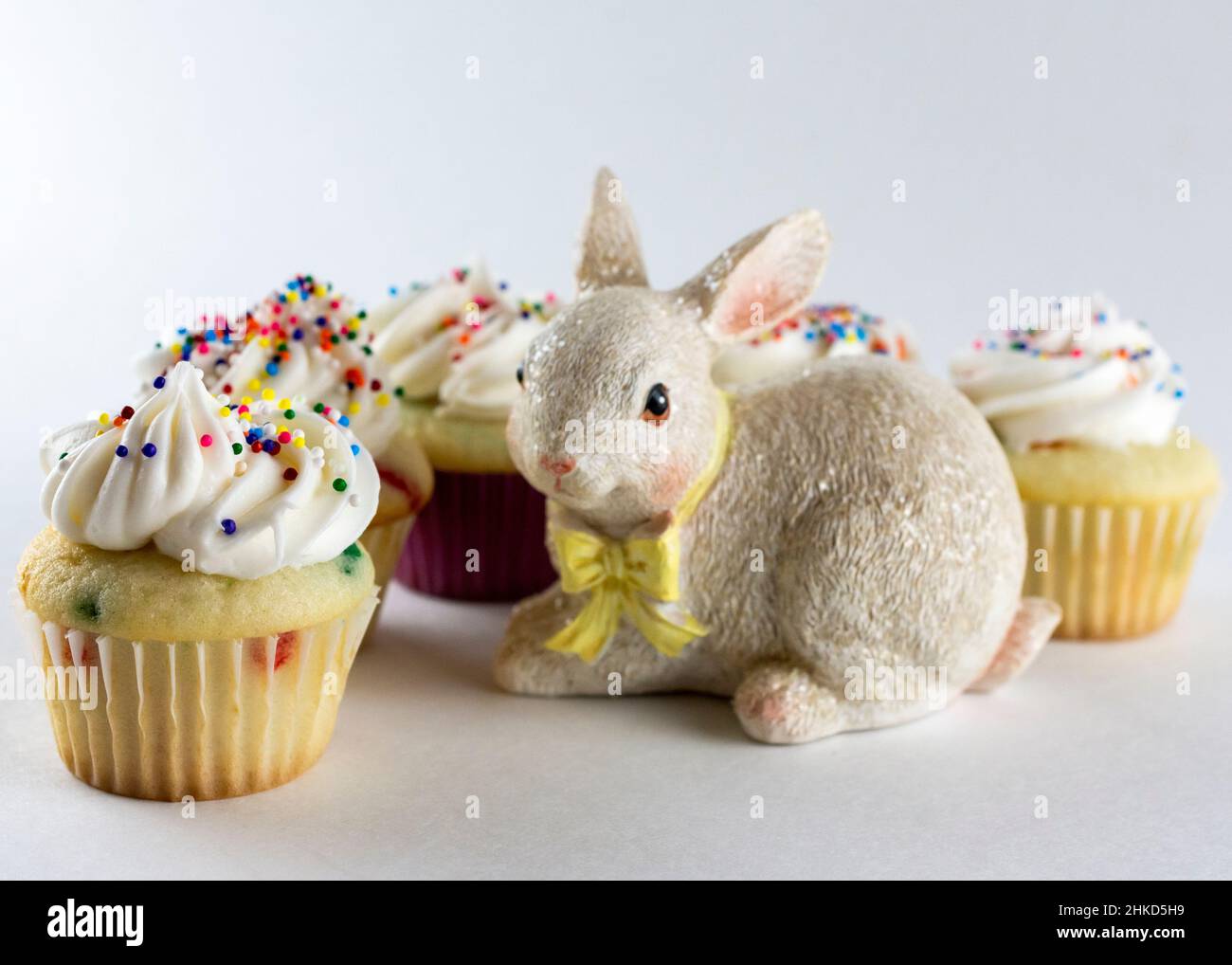 Petits gâteaux de couleur ressort disposés autour d'une figurine de lapin.Concentrez-vous sur la plupart des cupcakes à l'avant avec un flou supplémentaire en arrière-plan.Fond blanc Banque D'Images