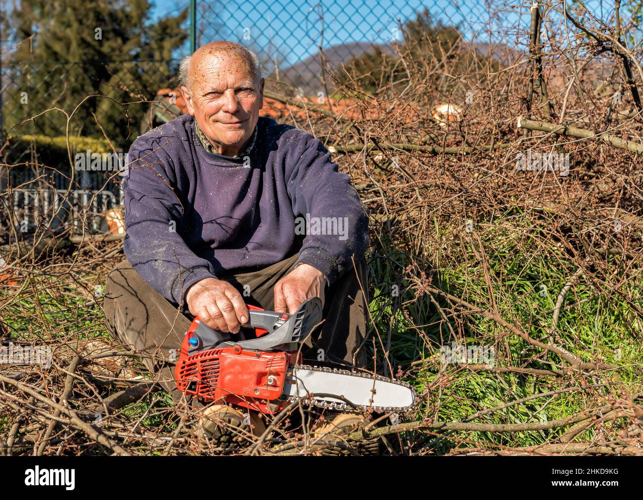Homme senior heureux avec tronçonneuse assis pour se reposer après avoir coupé l'arbre dans le jardin Banque D'Images