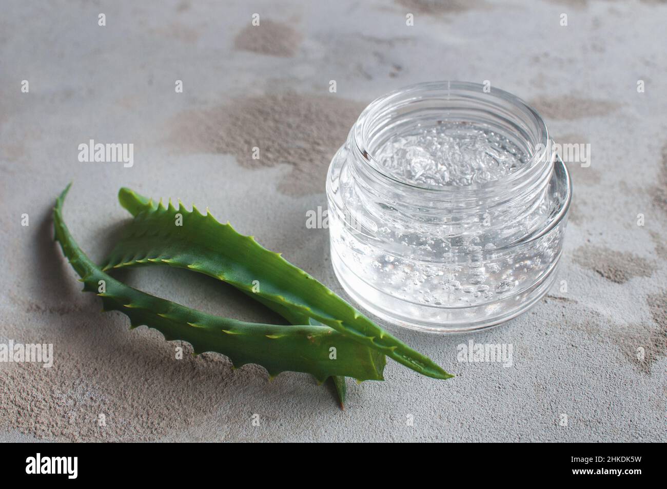 Texture de gel avec des bulles d'acide hyaluronique et des branches d'aloe vera dans un pot de verre sur un fond de béton Banque D'Images