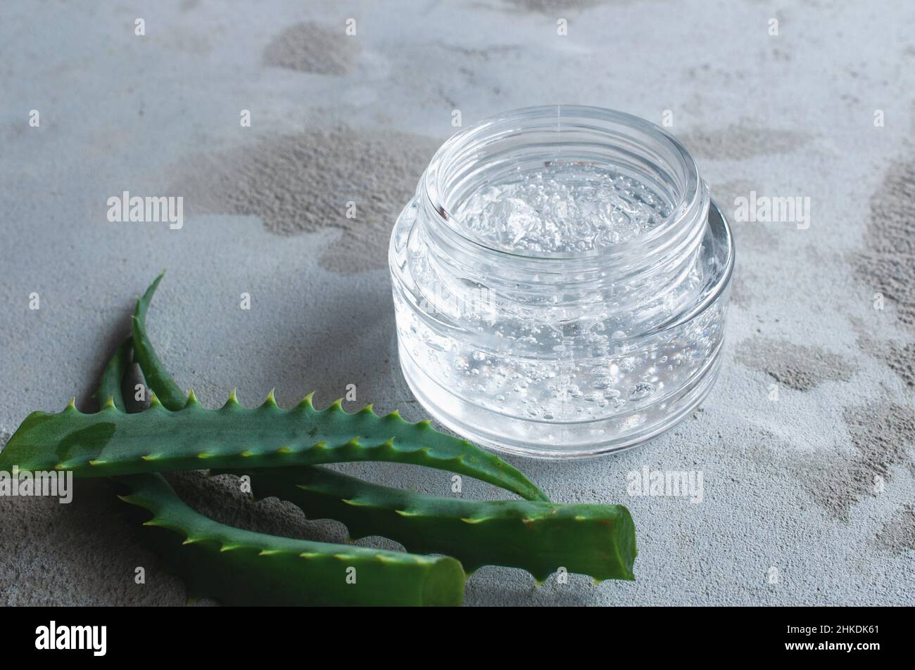 Texture de gel avec des bulles d'acide hyaluronique et des branches d'aloe vera dans un pot de verre sur un fond de béton Banque D'Images