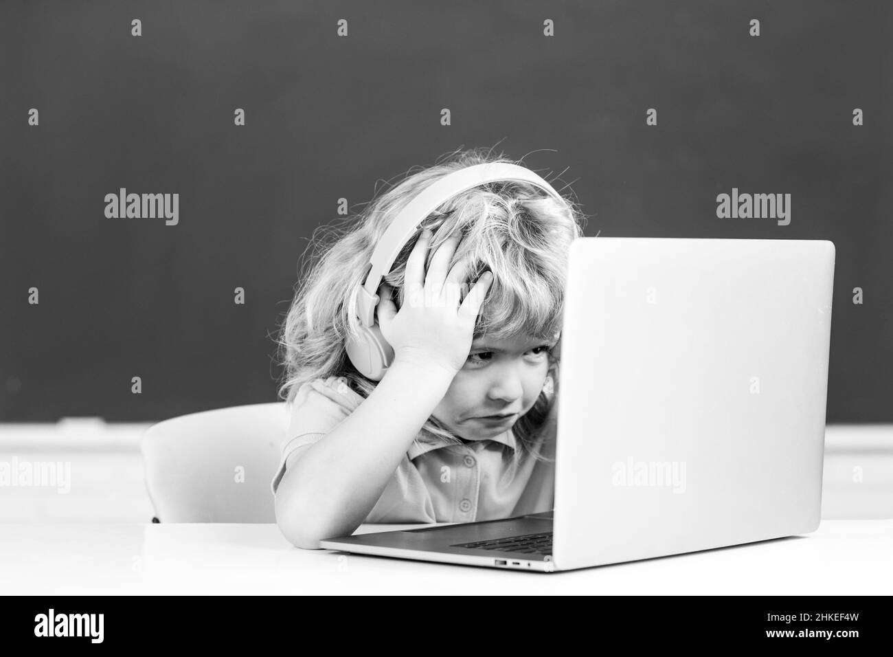 Un garçon triste en colère portant un casque, étudier avec un ordinateur portable en classe, cours de cours sur l'écoute audio. Banque D'Images