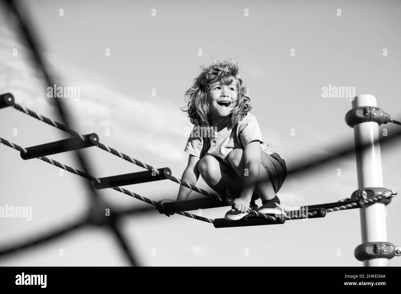 Un adorable garçon monte sur l'échelle de l'aire de jeux.L'enfant monte l'échelle contre le ciel bleu.Copier l'espace pour le texte. Banque D'Images