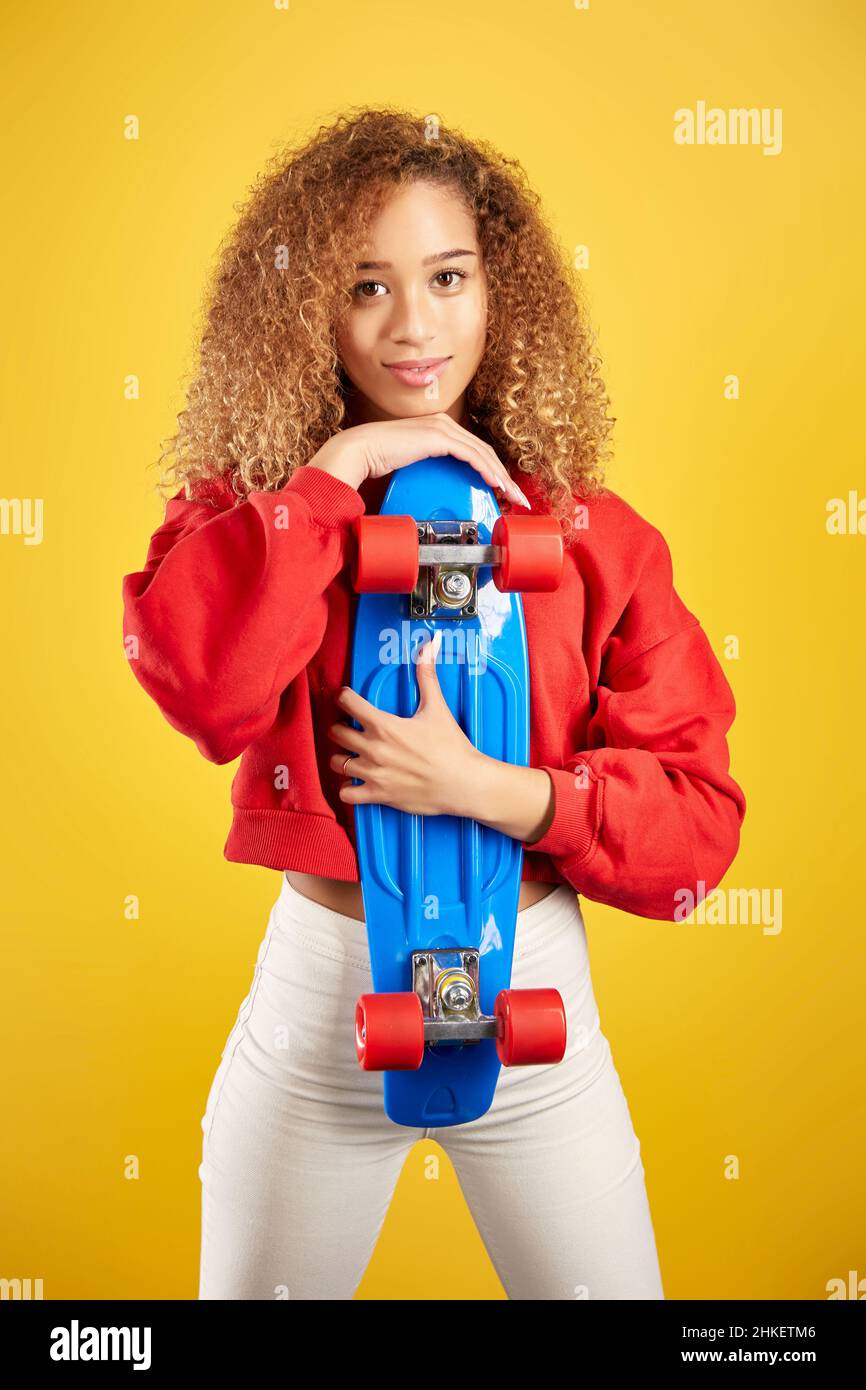 Ravie de jeunes Afro-américaines hipster dans le sweat à capuche et avec panneau de penny regardant la caméra sur fond jaune Banque D'Images