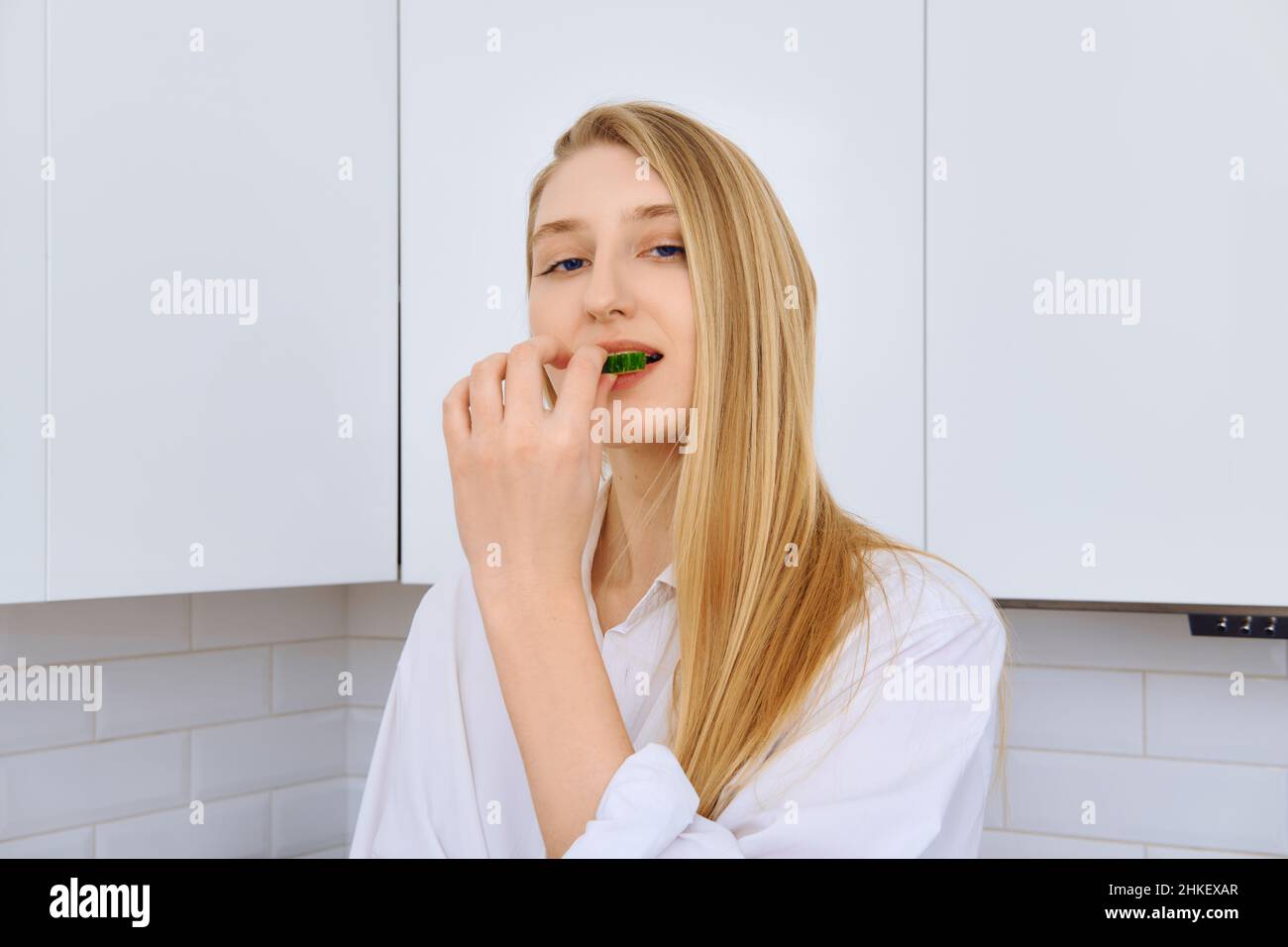 Une femme délicate mord un morceau de concombre tout en faisant de la salade de légumes Banque D'Images