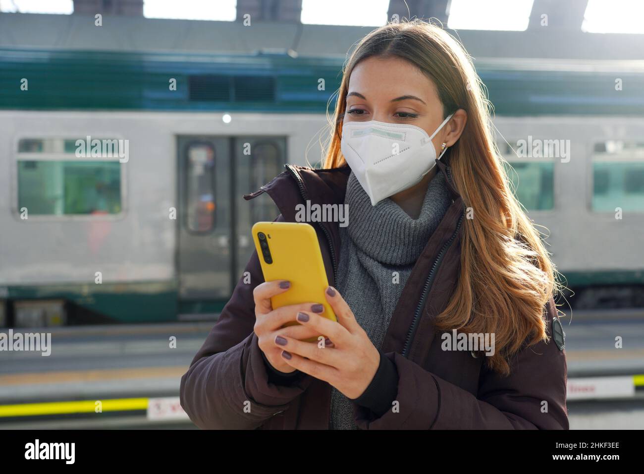 Jeune femme avec masque médical acheter un billet en ligne avec smartphone à la gare Banque D'Images