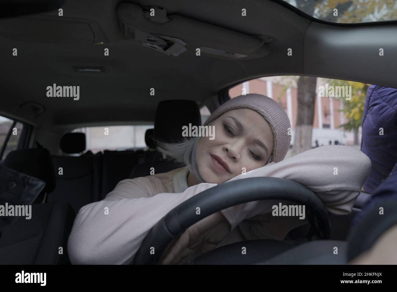 Femme asiatique fatiguée dormant dans la voiture.Une femme asiatique mûre s'est endormie à la voiture sur un volant.Femme asiatique blonde d'âge moyen dans la voiture.Femme sur la route.Concept d'entreprise. Banque D'Images
